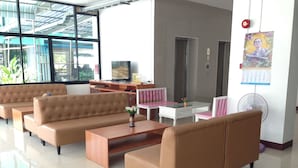 Un hall d’entrée moderne avec des canapés en cuir, une table basse en bois, une table en verre surmontée de chaises roses, un téléviseur, un calendrier et un ventilateur.