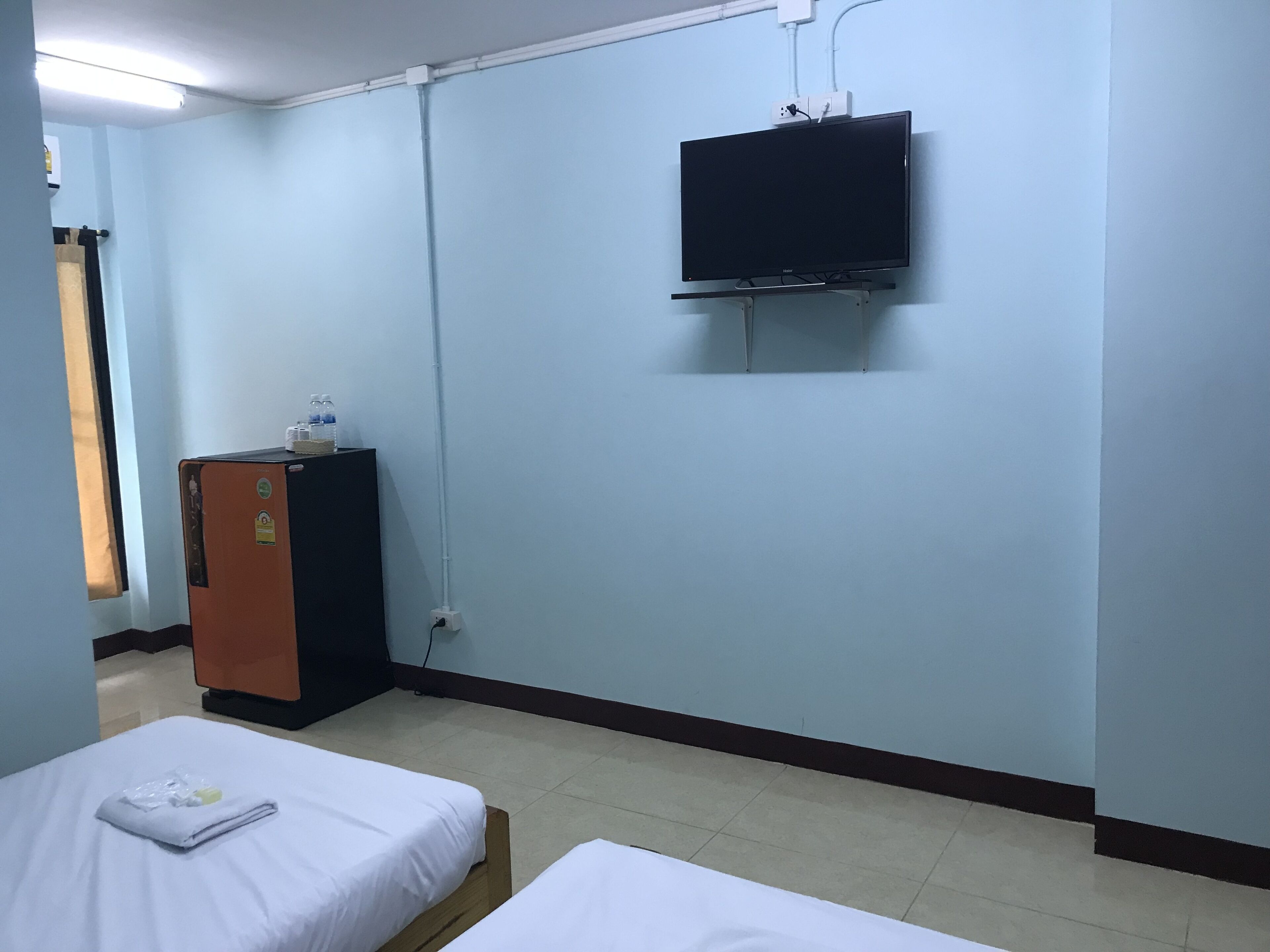 A hotel room with two beds, a TV mounted on the wall, and a small cabinet with a water bottle on top.