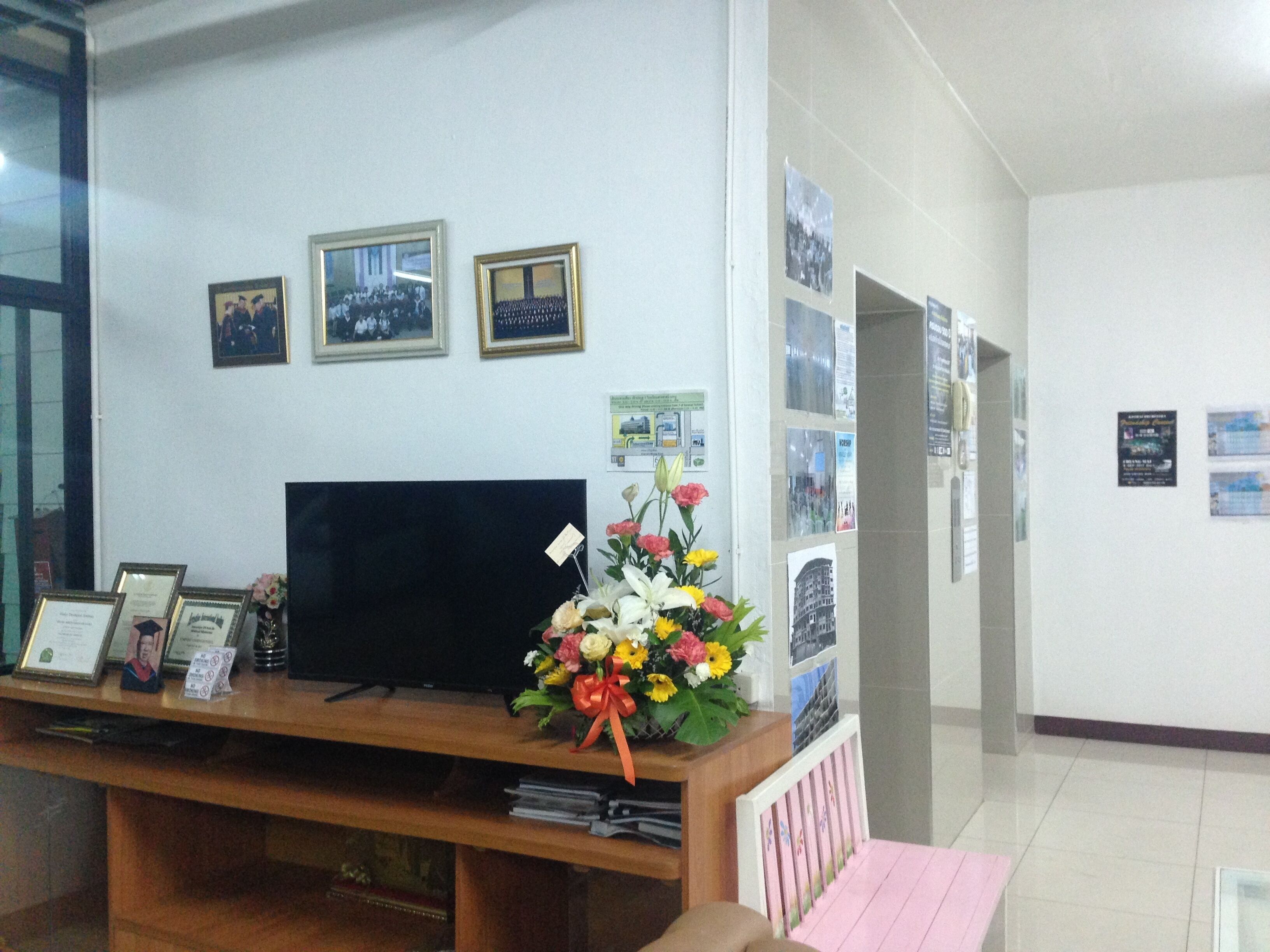 Zona de recepción con un mostrador de madera, cuadros en la pared, un televisor y un arreglo floral.