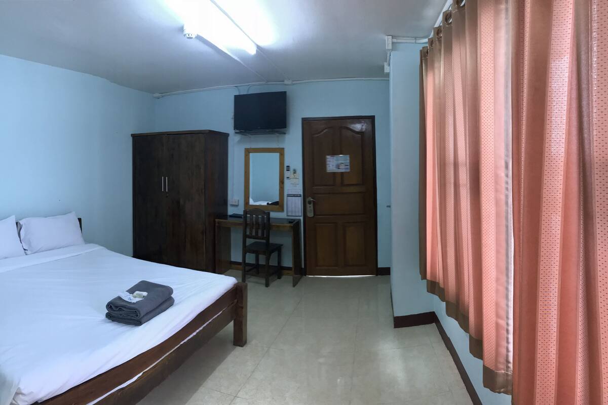 A bedroom with a bed, a desk, a chair, a wardrobe, a television, and a door.