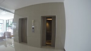 Un couloir avec deux portes, un interphone fixé au mur et un sol carrelé.