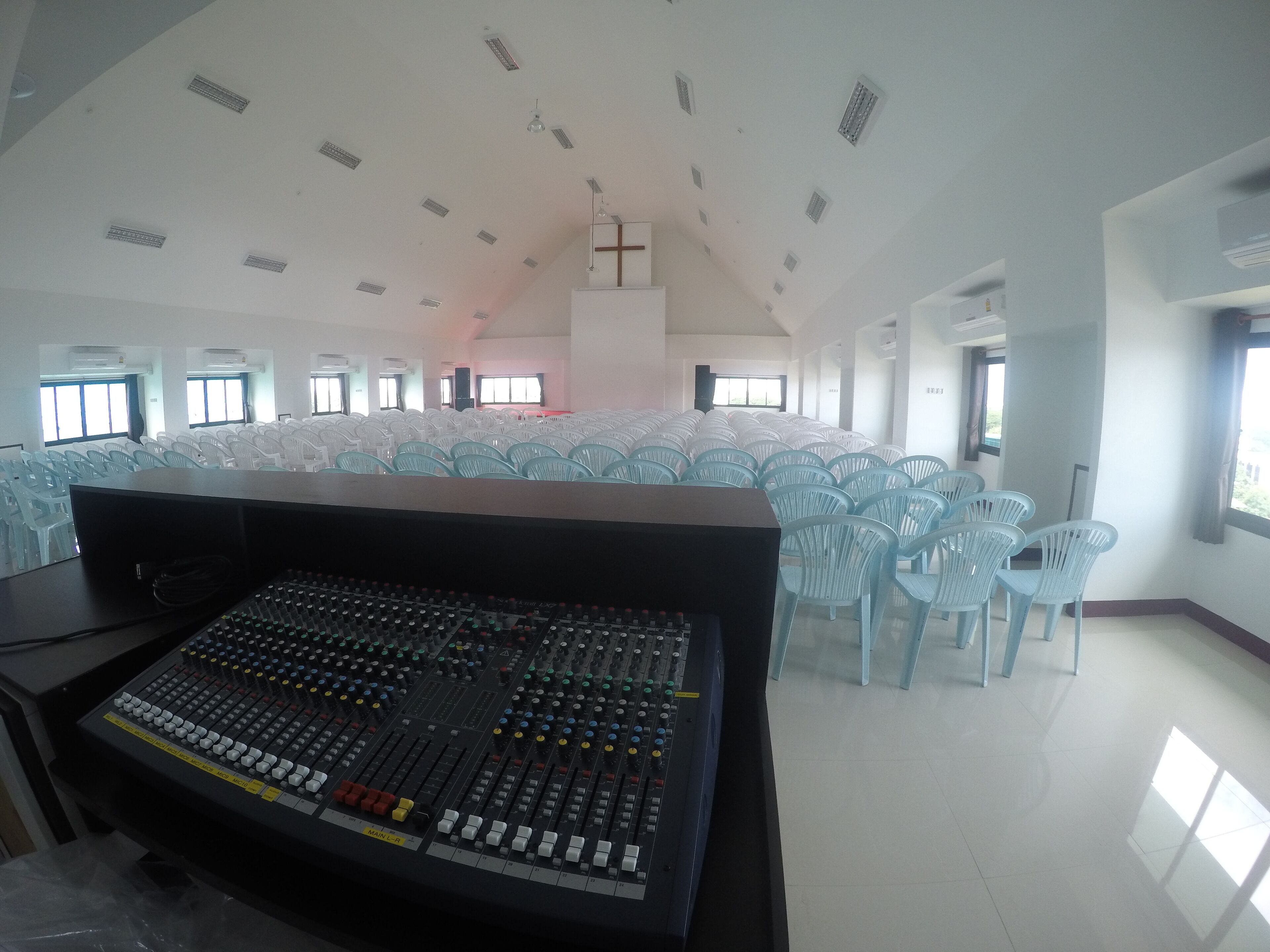 A large hall with rows of chairs, a sound mixing console, and a cross on the ceiling.