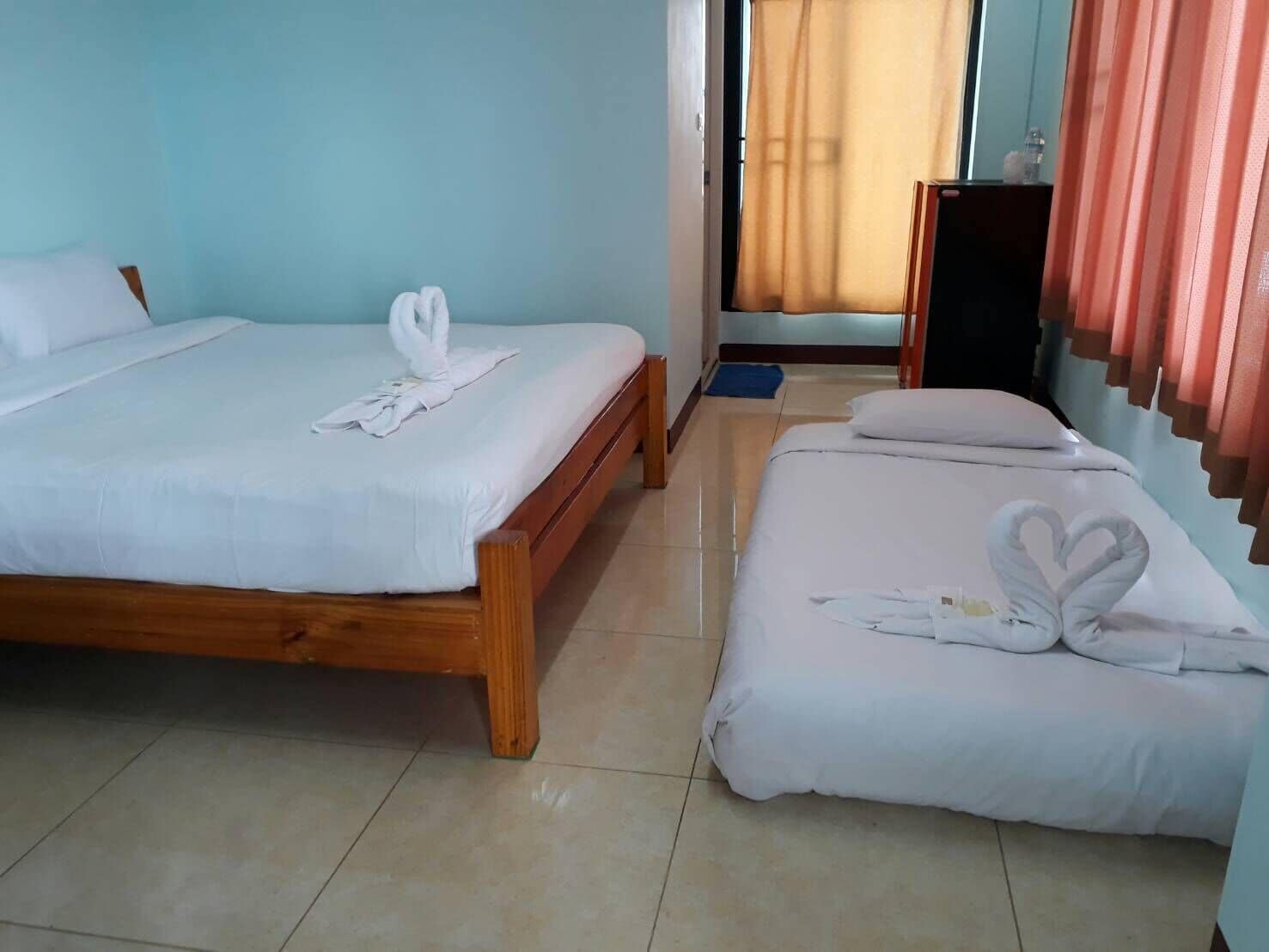 Una camera d'albergo con due letti, uno più grande e uno più piccolo, entrambi con lenzuola e asciugamani disposti a forma di cuore.