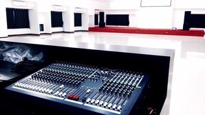 Une salle de contrôle équipée de matériel de mixage sonore, un tapis rouge et des rideaux noirs aux fenêtres.