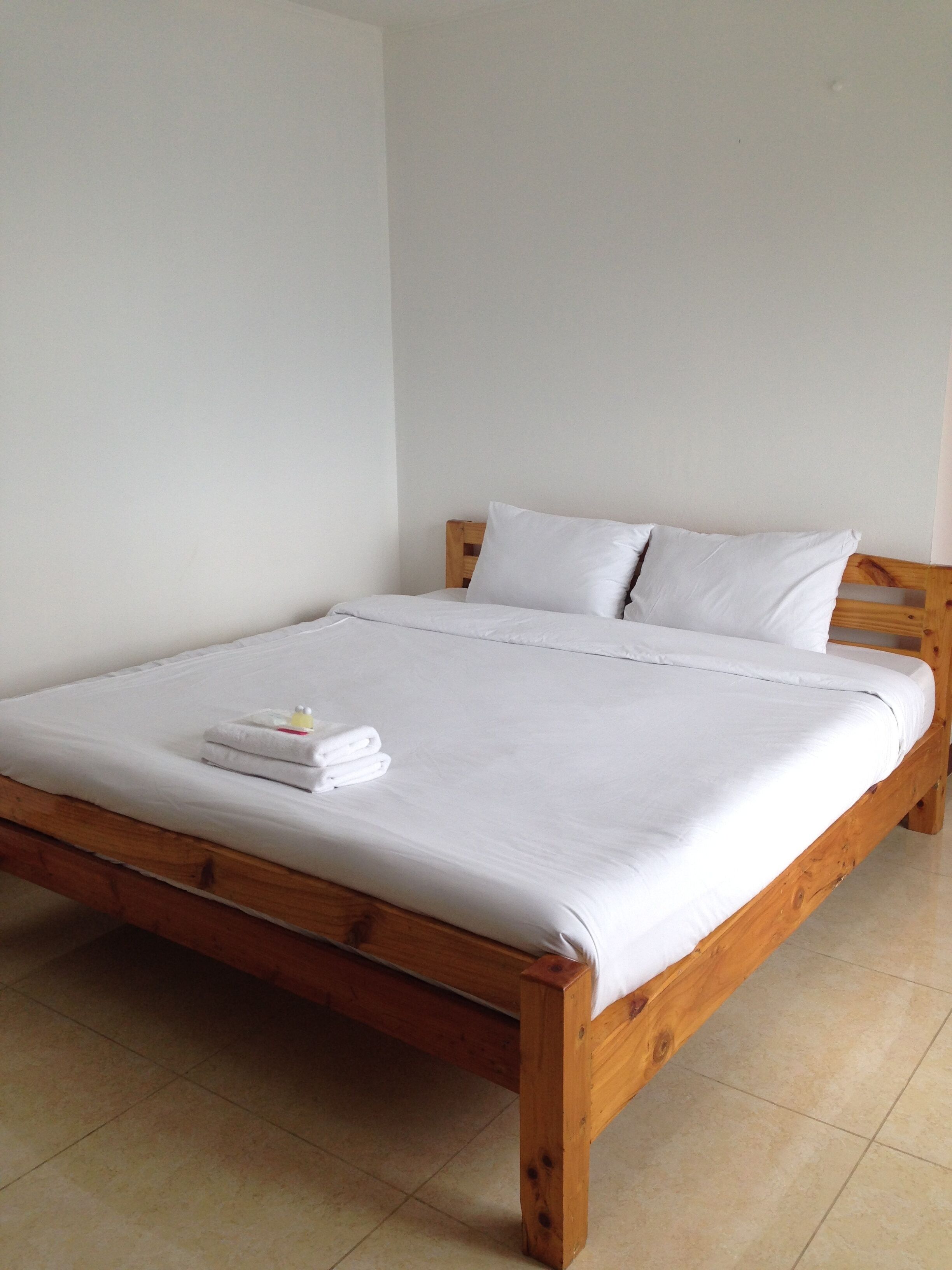 Uma cama de solteiro com roupa de cama e almofadas brancas, cabeceira de madeira e uma toalha pequena sobre a cama.