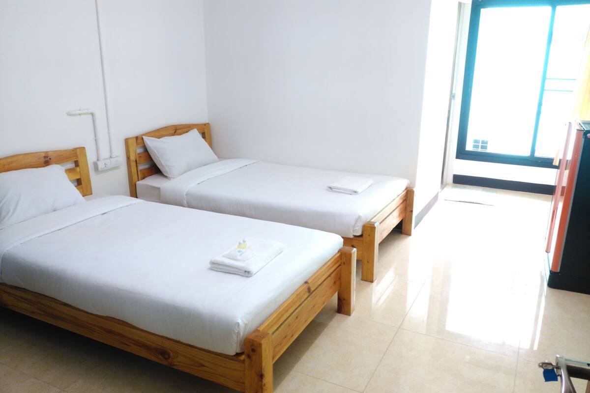 Two wooden beds with white linens in a room with a tiled floor and a window.