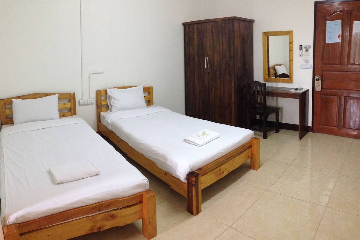 Two wooden beds with white linens, a wooden wardrobe, a desk with a chair, and a door with a mirror and a sign.