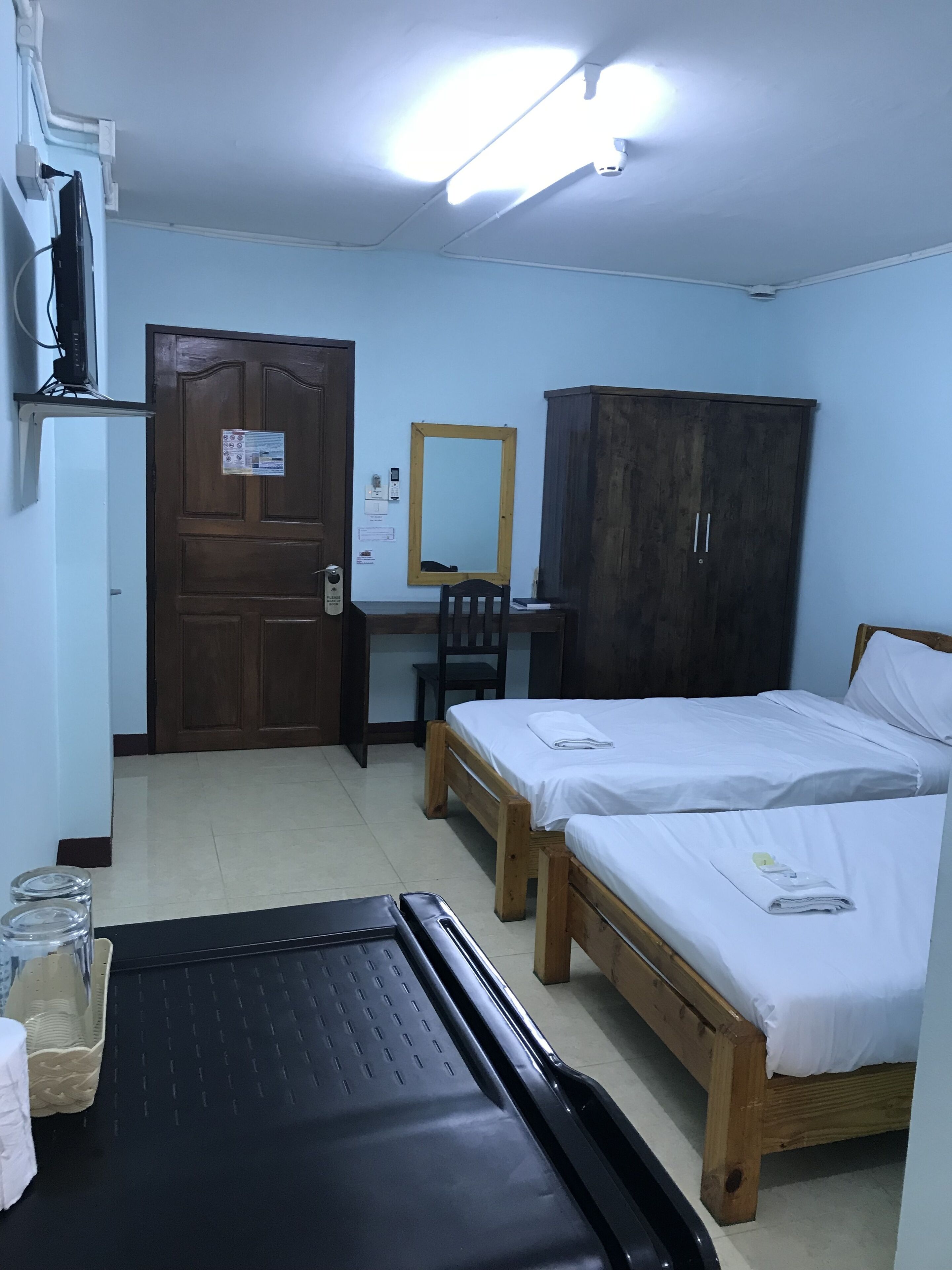 A room with two wooden beds, a desk with a chair, a wardrobe, a door with a notice, and a black mat on the floor.
