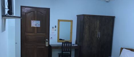 A room with two wooden beds, a desk with a chair, a wardrobe, a door with a notice, and a black mat on the floor.