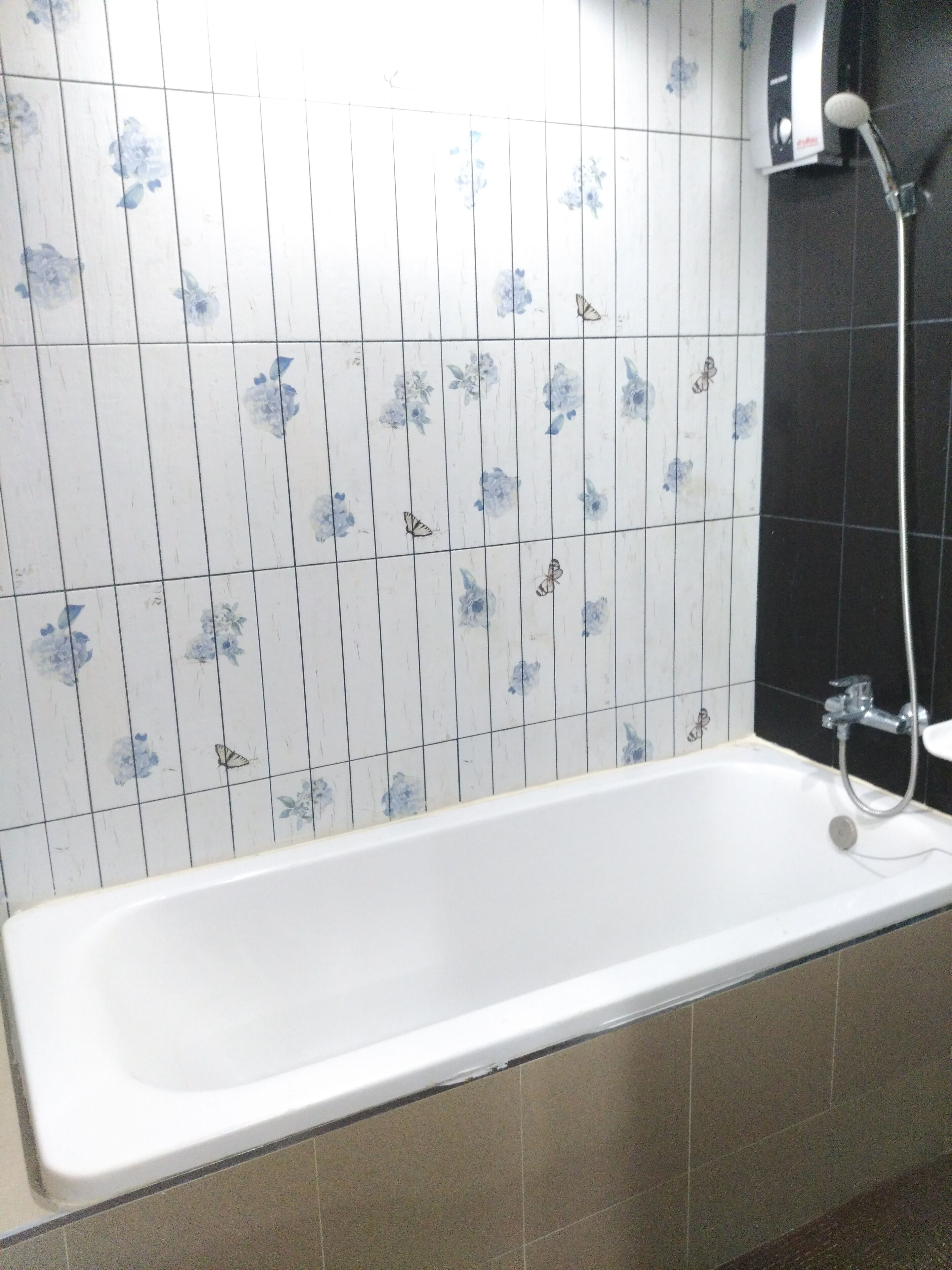 A bathroom with a bathtub, a shower, and floral-patterned tiles.