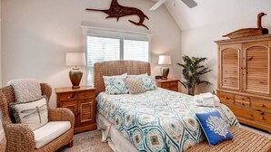 A bedroom with a bed, a chair, a nightstand, a lamp, a cabinet, and a ceiling fan.