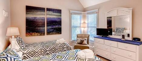 A bedroom with a bed, a dresser, a TV, and artwork on the wall.