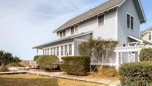A two-story house with a covered porch and a wooden deck. - Bonnie Doon 2 Bedroom Holiday Home By Bald Head Island (Bald Head Island)