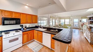 A modern kitchen with wooden cabinets, a black microwave, white stove, and a black countertop. - Bonnie Doon 2 Bedroom Holiday Home By Bald Head Island (Bald Head Island)