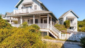 A two-story house with a porch, a staircase, and a white picket fence. - Blue Heron 3 Bedroom Holiday Home By Bald Head Island (Bald Head Island)