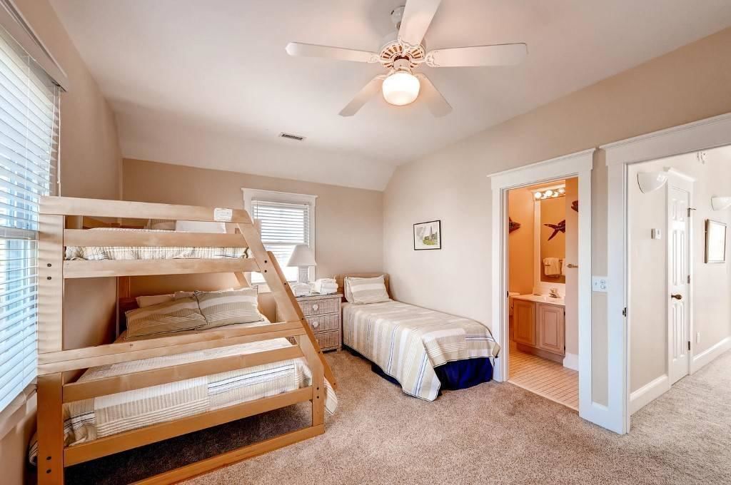 A bedroom with bunk beds, a single bed, a ceiling fan, and a bathroom visible through an open door.