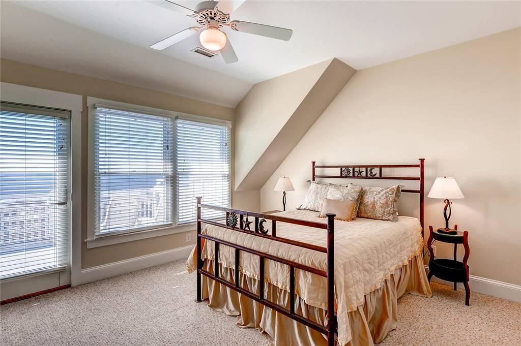 A bedroom with a wooden bed, two bedside lamps, a ceiling fan, and large windows with blinds.