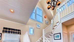 A spacious interior with a staircase, a chandelier, and a large window providing natural light. - Bogan s on the Beach 4 Bedroom Holiday Home By Bald Head Island (Bald Head Island)
