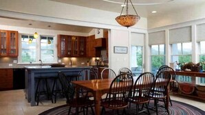 A modern kitchen with wooden cabinets, a central island, and a dining area with a round table and chairs. - Cape Watch Cottage 4 Bedroom Holiday Home By Bald Head Island (Bald Head Island)