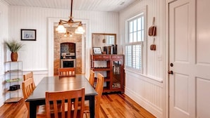 A dining area with a wooden table and chairs, a brick fireplace, and a white paneled wall. - Captain Charlie s 1 3 Bedroom Holiday Home By Bald Head Island (Bald Head Island)