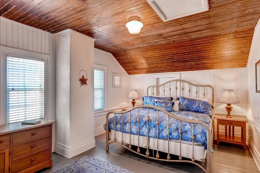 A bedroom with a wooden ceiling, a bed with a metal frame, two bedside tables, and a window with blinds.
