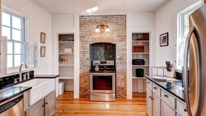 A kitchen with white paneling, a brick fireplace, stainless steel appliances, and wooden flooring. - Captain Charlie s 1 3 Bedroom Holiday Home By Bald Head Island (Bald Head Island)