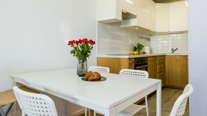 Une cuisine moderne avec des meubles blancs, un plan de travail blanc et un coin repas comprenant une table et des chaises blanches.