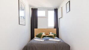 Un lit bien fait, recouvert d’une couverture à rayures grises, avec deux oreillers et un plateau sur lequel se trouvent une tasse et un croissant.