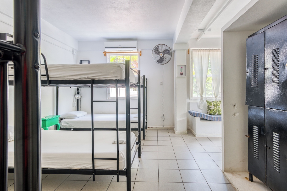 Un dormitorio con literas, un ventilador, una ventana con cortinas y un armario.