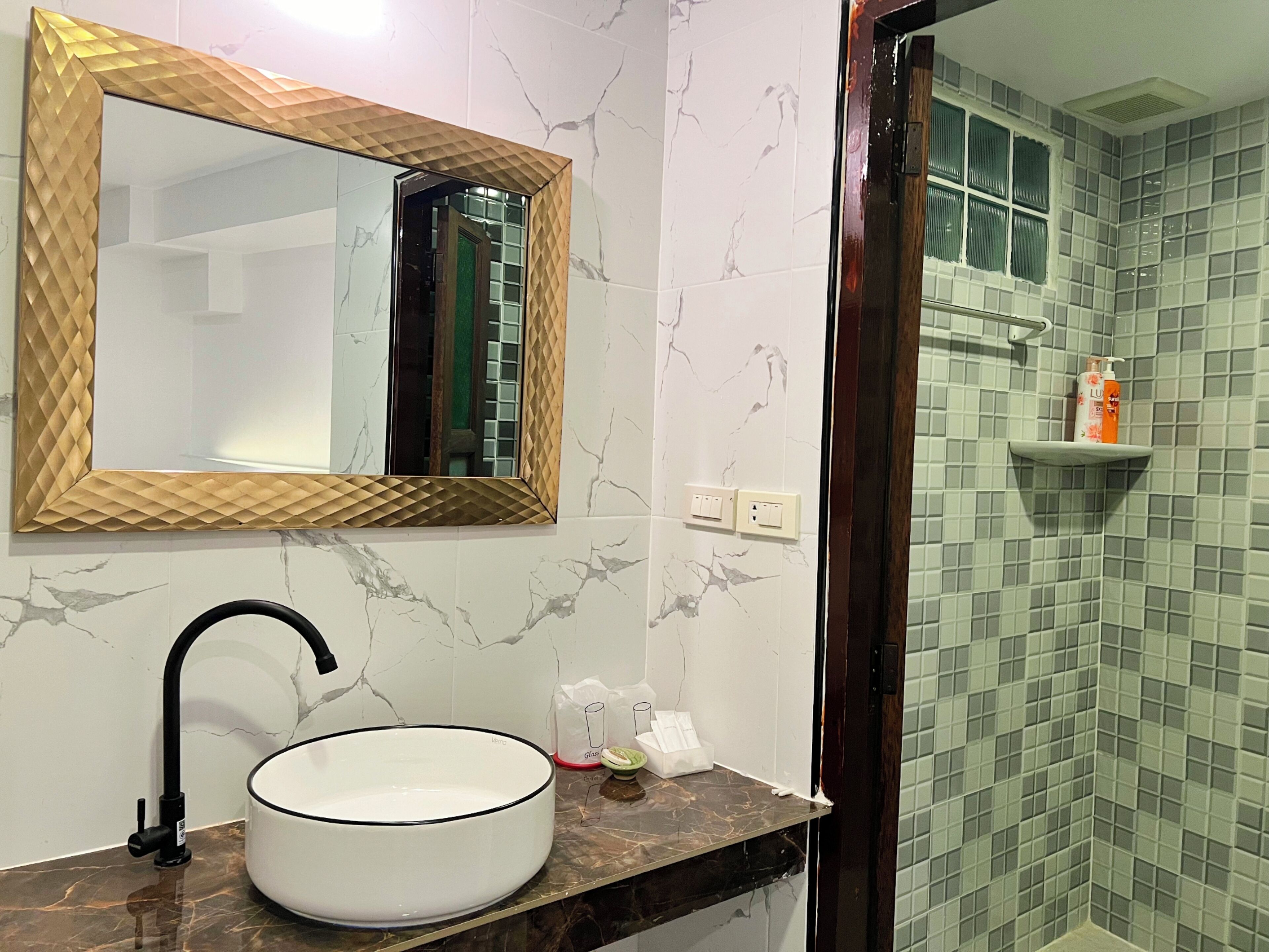 A bathroom with a white sink, a mirror with a wooden frame, and a shower area with green tiles.
