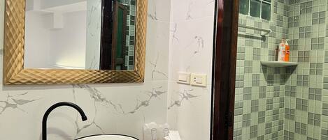 A bathroom with a white sink, a mirror with a wooden frame, and a shower area with green tiles.