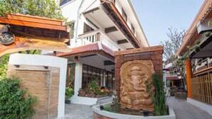 A courtyard with a stone statue, a brick wall, and a building with a red roof. - Somwang Boutique House (Chiang Mai)