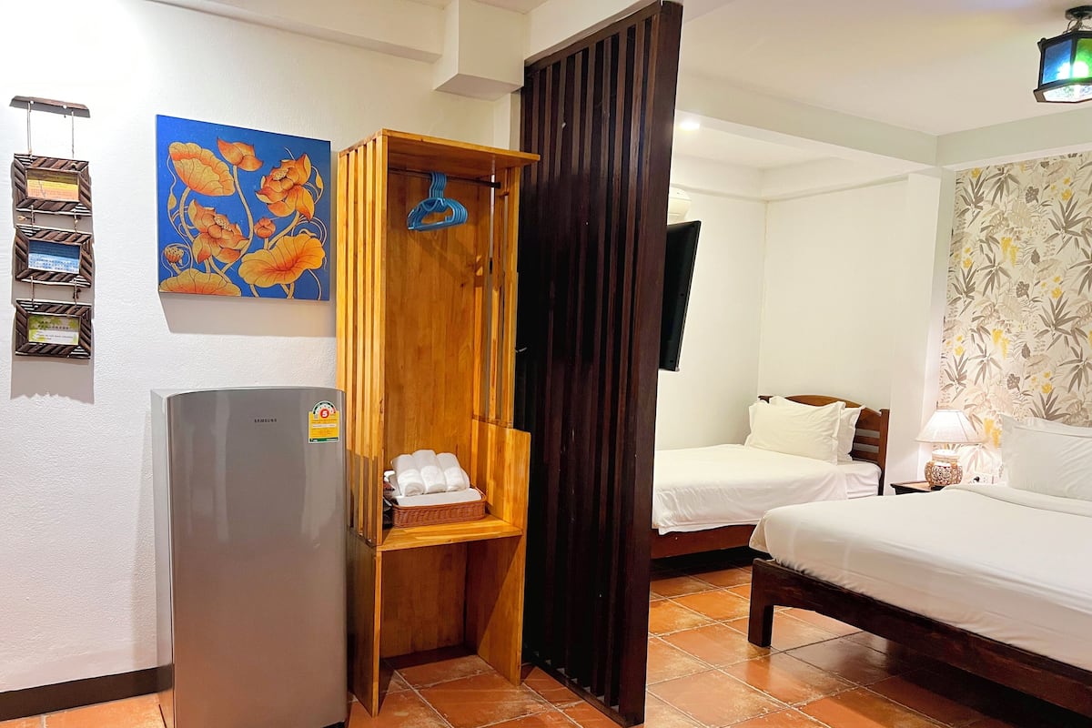Une chambre d’hôtel avec un lit, une armoire en bois contenant des serviettes, un réfrigérateur, un téléviseur fixé au mur et un papier peint à motifs floraux.