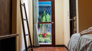 Un pasillo estrecho con una puerta de madera que da a un balcón lleno de plantas y flores en macetas.