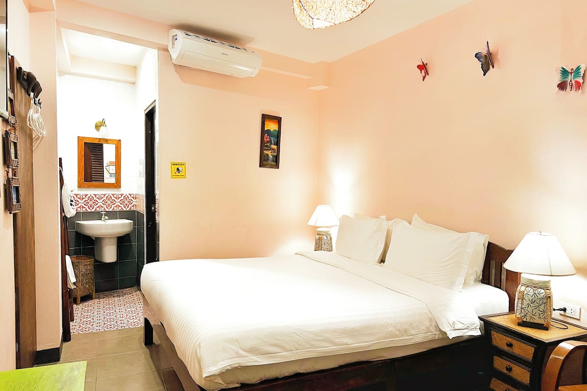 Une chambre à coucher comprenant un lit, des lampes de chevet, une table de chevet, un climatiseur mural, un lavabo et une porte donnant sur une autre pièce.