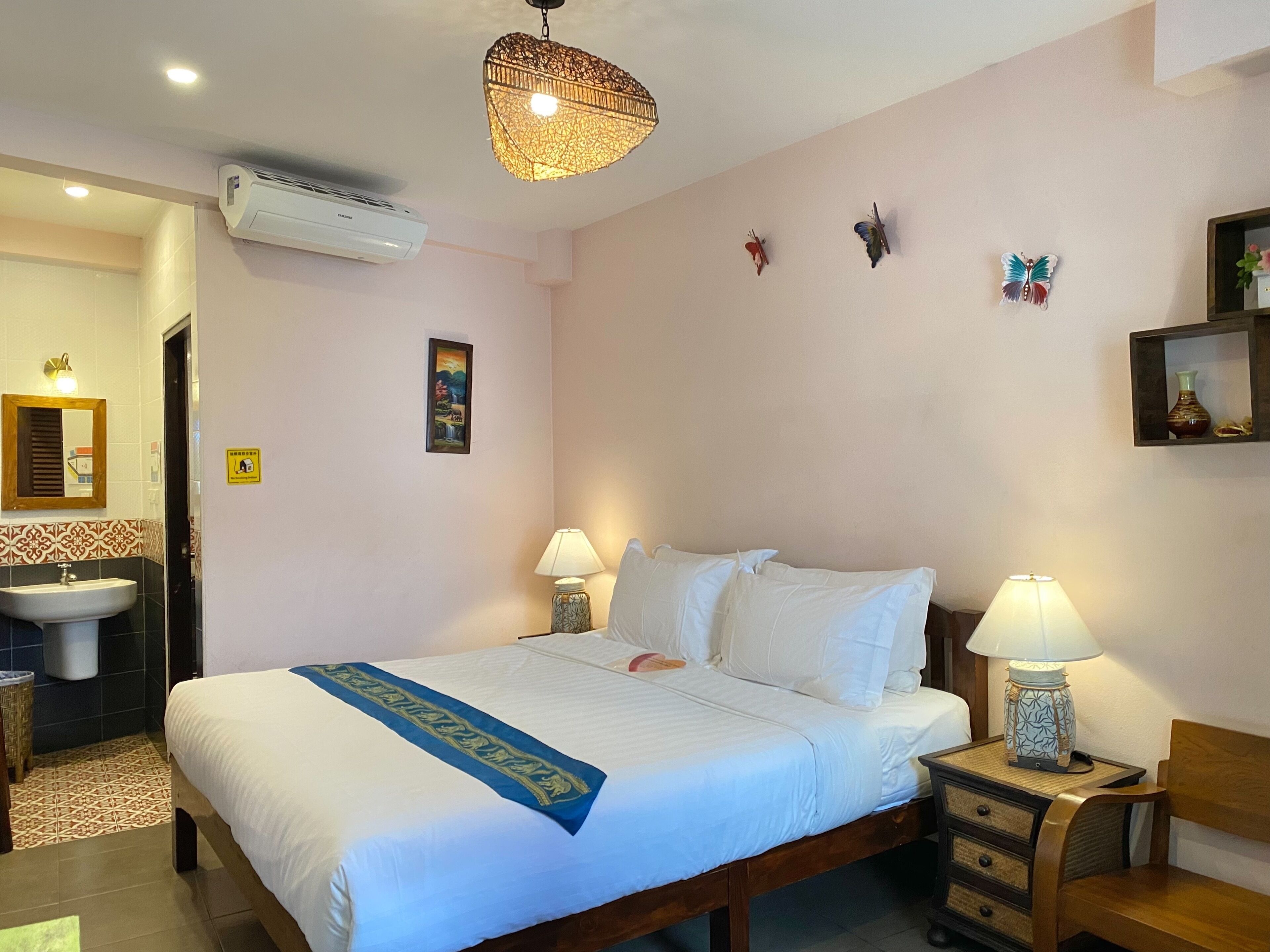 A hotel room with a bed, bedside lamps, a bedside table, a mirror, a sink, and a decorative butterfly on the wall.