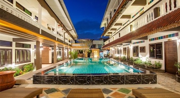 Un área de piscina con una piscina central, rodeada de sillas de descanso y plantas en macetas.