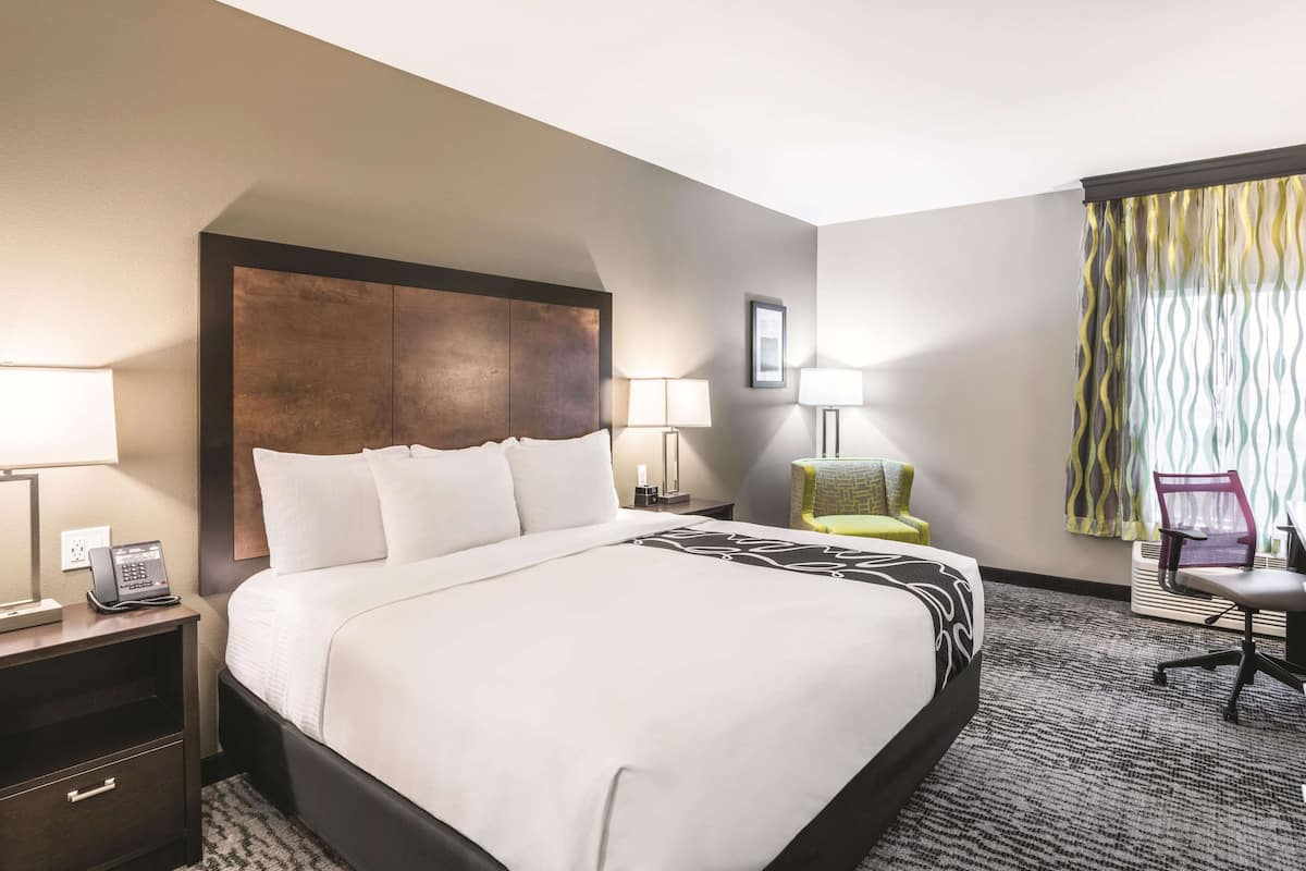 Habitación de hotel con una cama grande, lámparas de noche, un escritorio con teléfono, una silla y una ventana con cortinas.