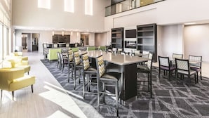 Une salle de conférence spacieuse, dotée de plusieurs tables et chaises, avec un coin cuisine à l’arrière et une mezzanine accessible par un garde-corps en verre.