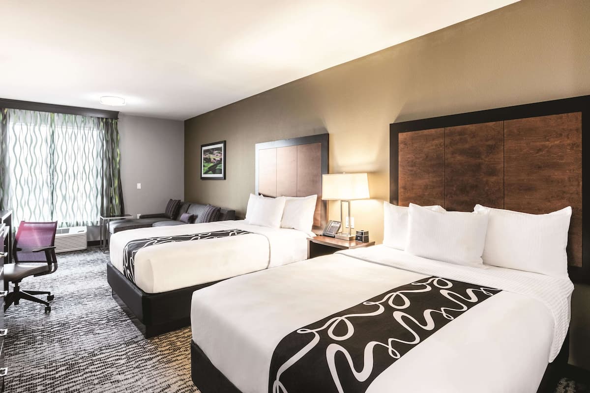 Habitación de hotel con dos camas, un escritorio, una silla y un ventanal con cortinas.
