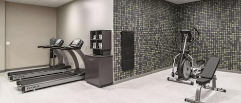 Un gimnasio con cintas de correr, una máquina elíptica y una banca para pesas.