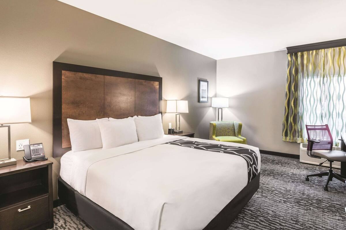 Una habitación de hotel con una cama grande, lámparas de noche, un escritorio con teléfono, una silla y una ventana con cortinas.