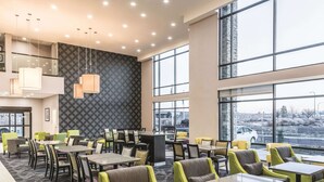 Un hall d’hôtel moderne doté de plusieurs espaces de détente, de grandes fenêtres et d’un mur orné de motifs.