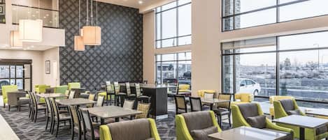 A modern hotel lobby with multiple seating areas, large windows, and a patterned wall.