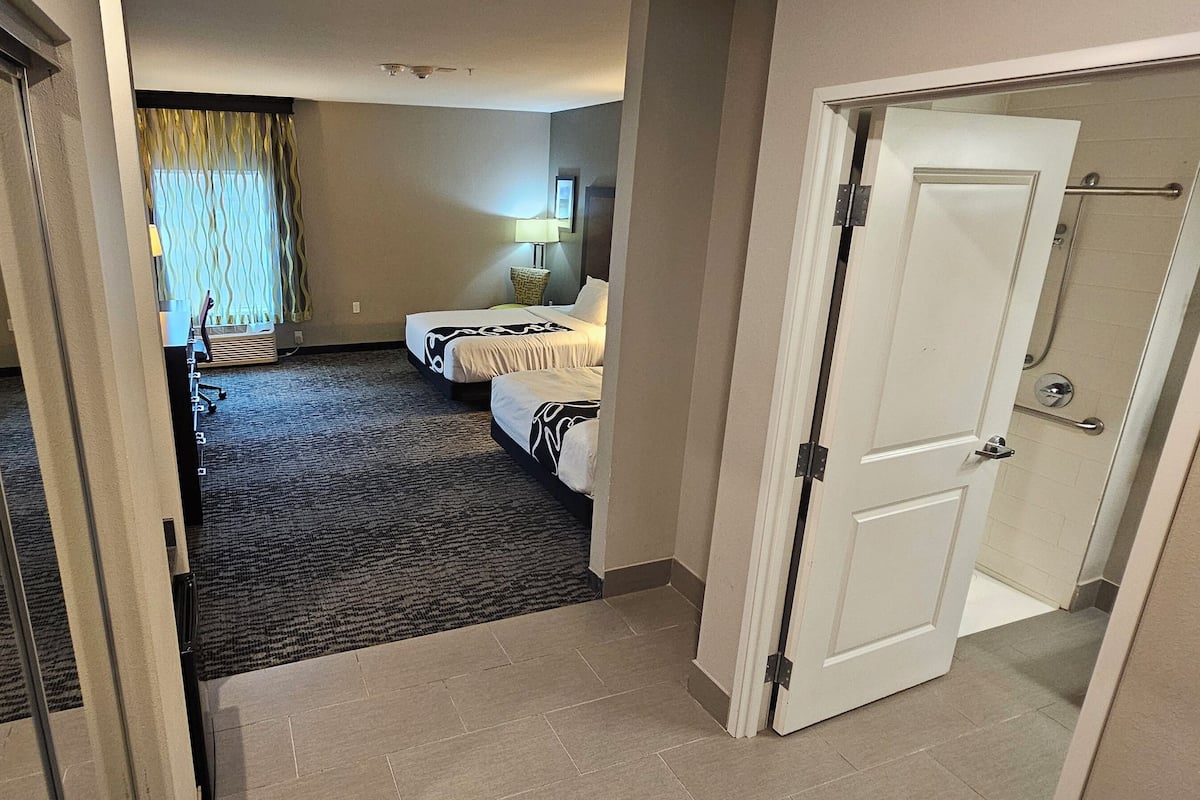 Habitación de hotel con dos camas, piso alfombrado, una puerta y zona de ducha.
