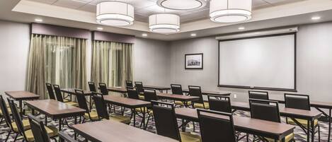 A conference room with multiple tables and chairs, a projector screen, and a patterned carpet.