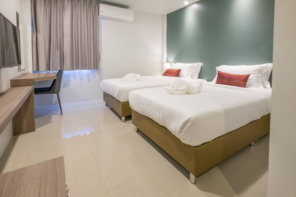 A hotel room with two beds, a desk, and a mirror.