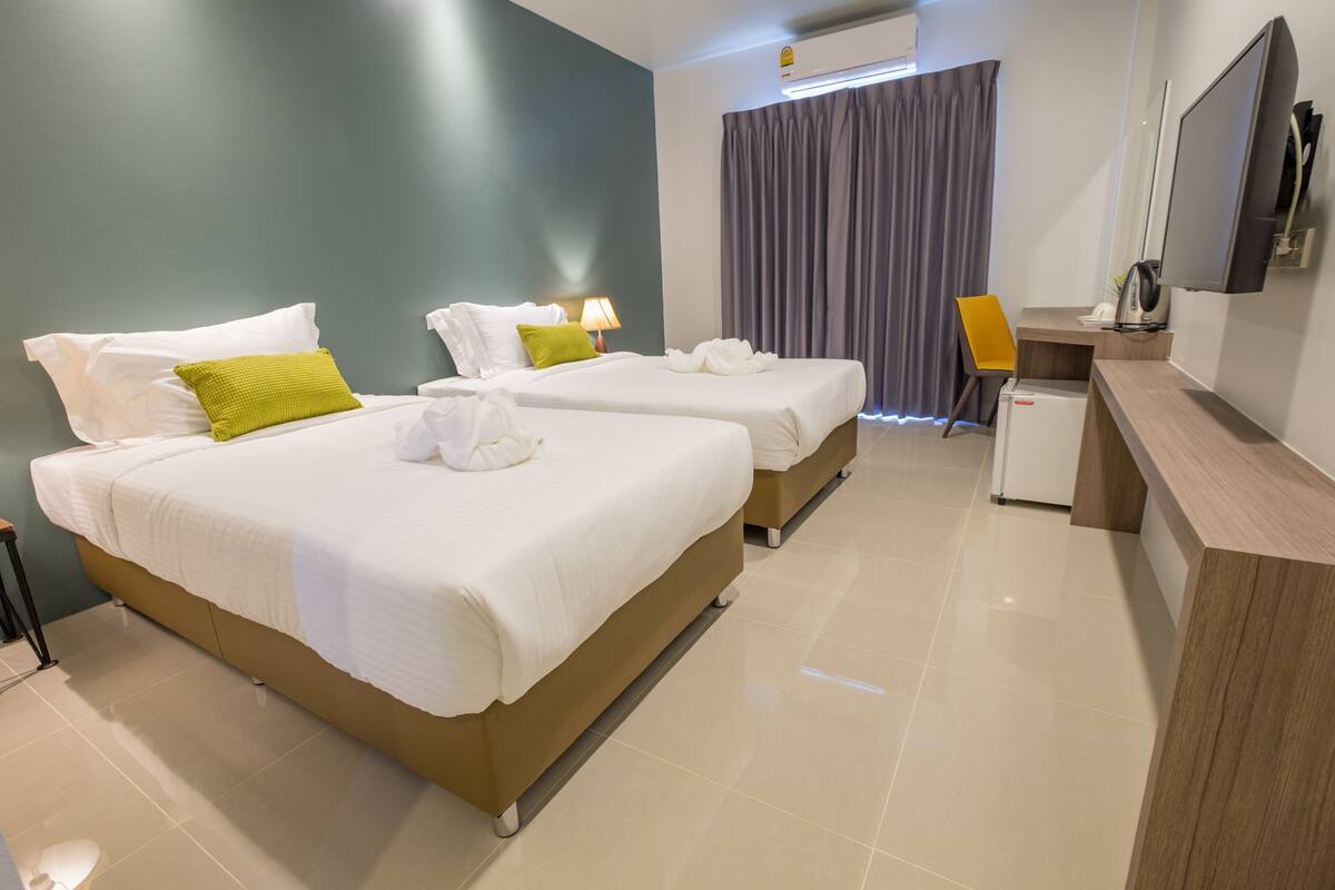 A hotel room with two beds, a desk, a chair, a TV, and a small refrigerator.