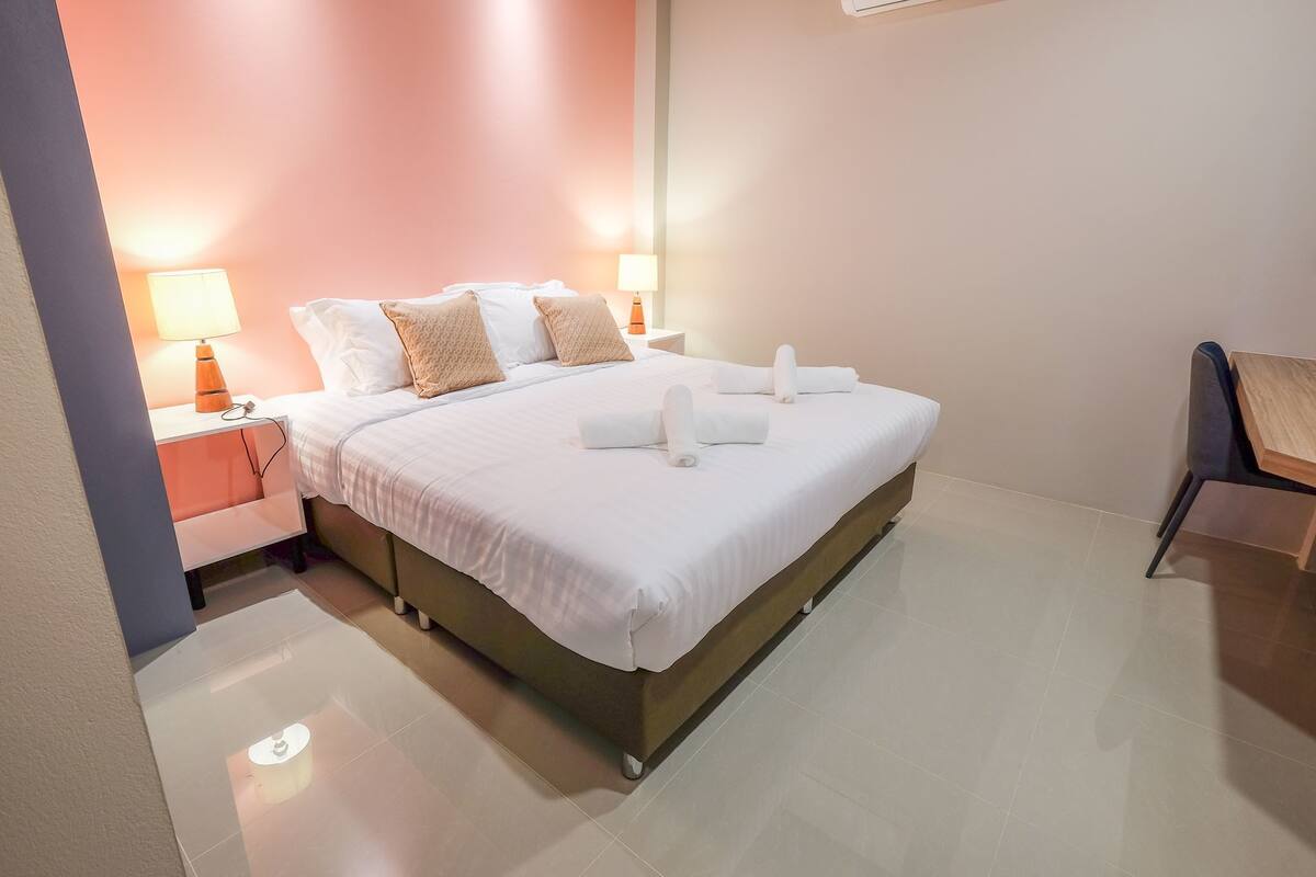 A neatly made bed with white linens and two towels, a bedside table with a lamp, and a chair in a modern hotel room.