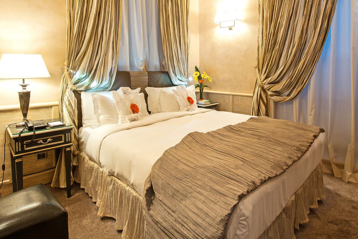 Habitación de hotel con una cama grande, una mesita de noche con lámpara, un teléfono y un jarrón con flores.